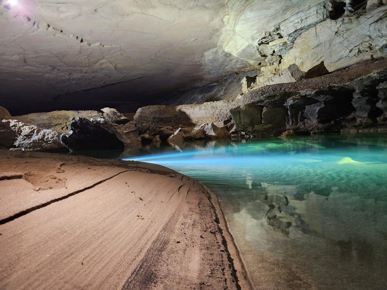 Underground pool with bright blue water and sandy cave bank